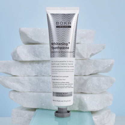A tube of Refresh Mint Whitening* n-Ha Toothpaste stands upright on stacked white marble slabs.