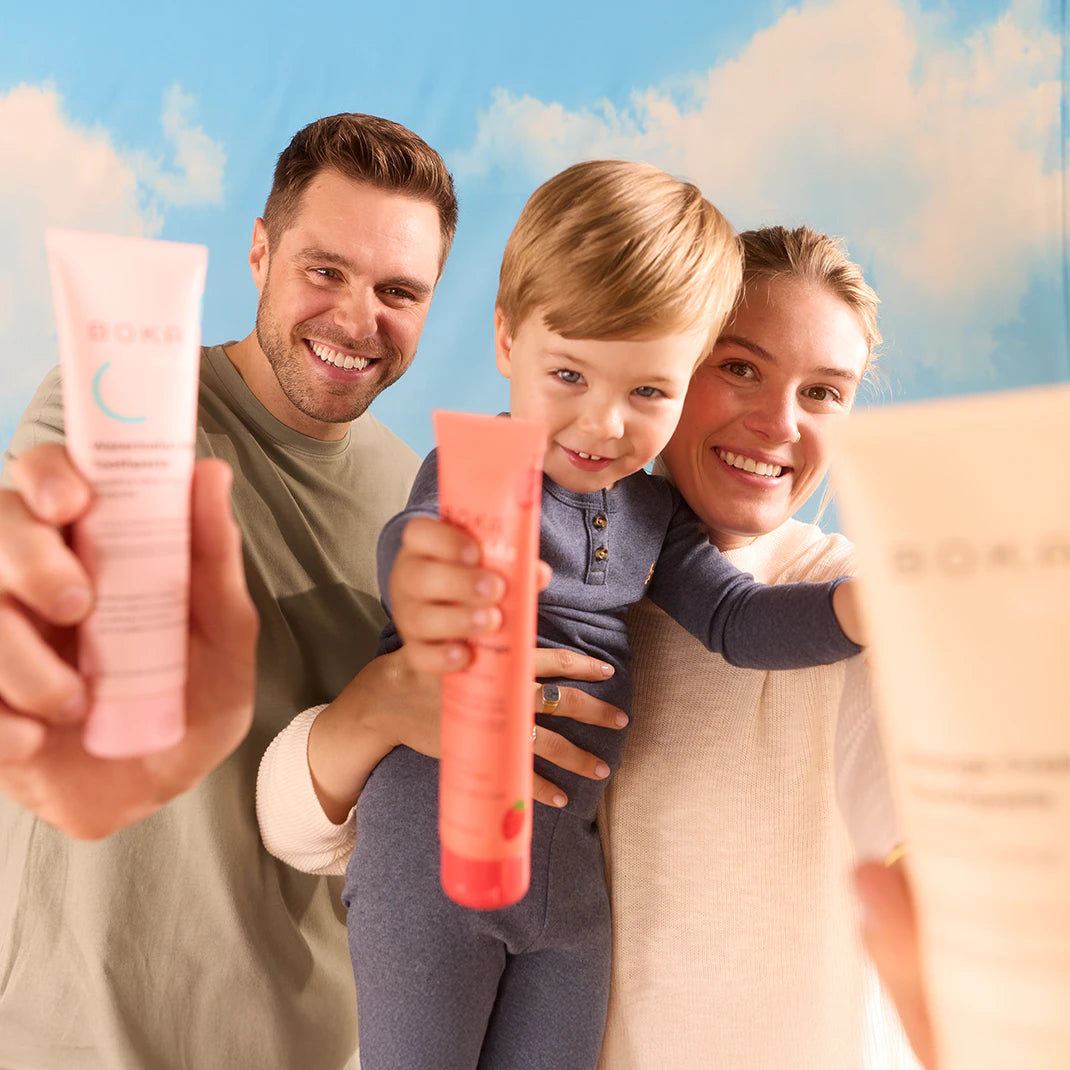 Smiling family poses together, each holding up tubes of personal care products toward the camera.