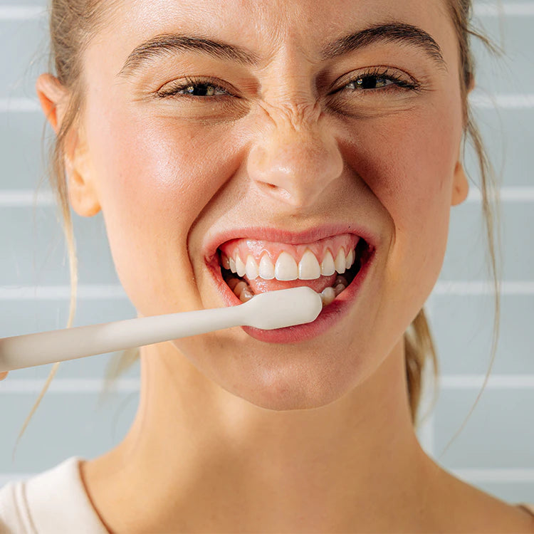 Woman smiling and brushing her teeth with a white toothbrush against a striped background.